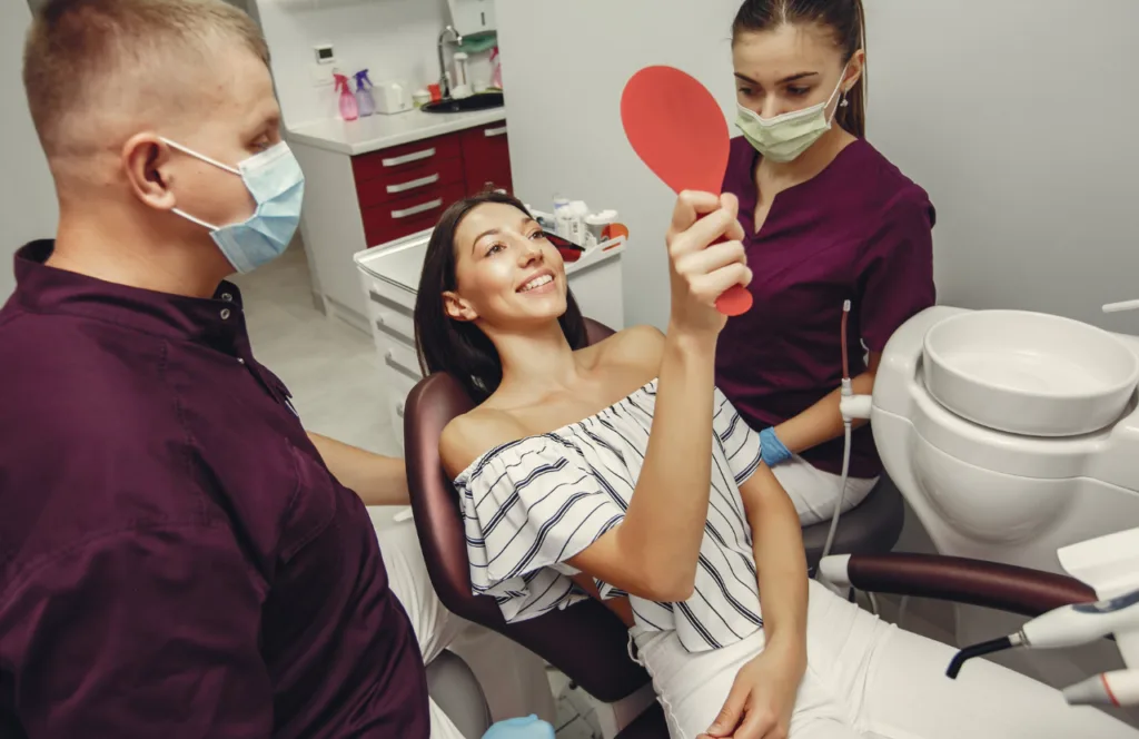 Dentist and dental assistant examining a smiling female patient during a dental consultation.